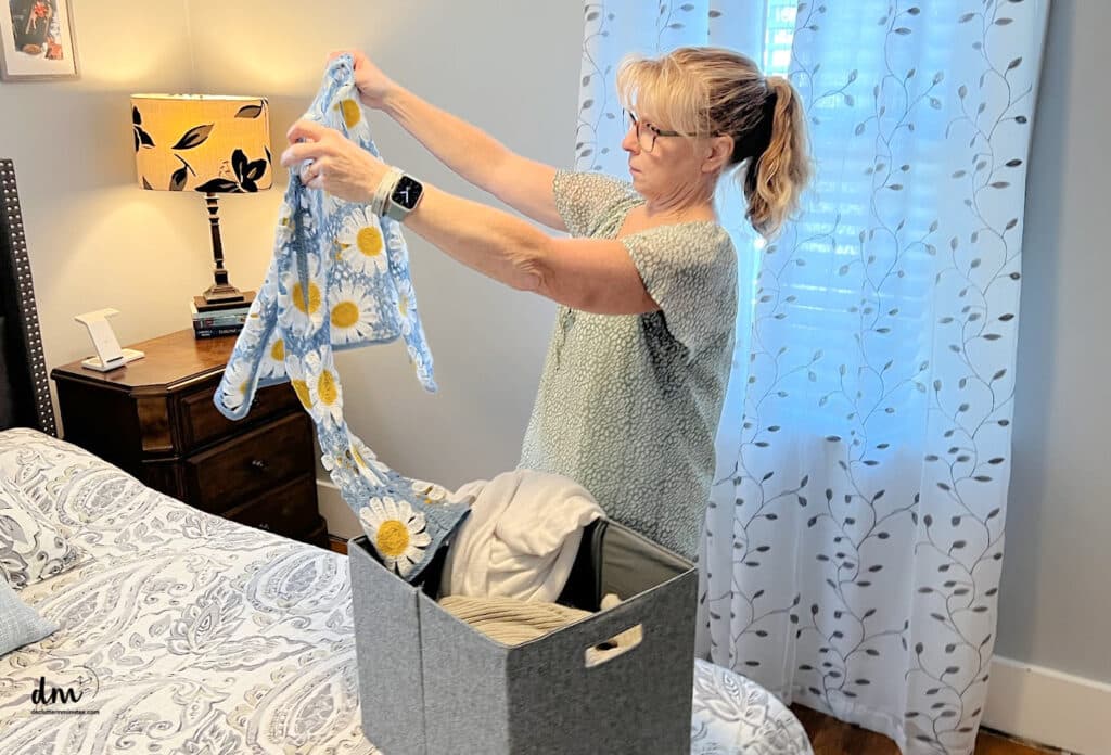 woman looking at a sweater in a bedroom deciding