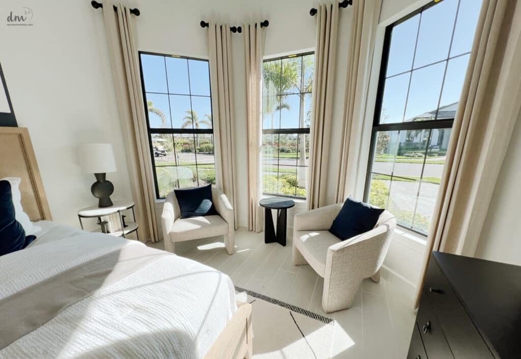 cozy neat and organized bedroom with 2 chairs in front of 3 large windows