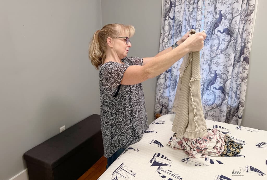 A woman looking at a sweater she is holding up questioning to keep it